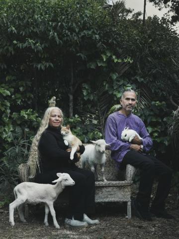 Retrato de Familia de Claudia y Luis, activistas por los derechos de los animales, sentados sobre un sofá en el exterior con las cotorras argentinas Cocota y Manolo, los corderos Ramón y Rafa, la gata Mona y el conejo Copito.